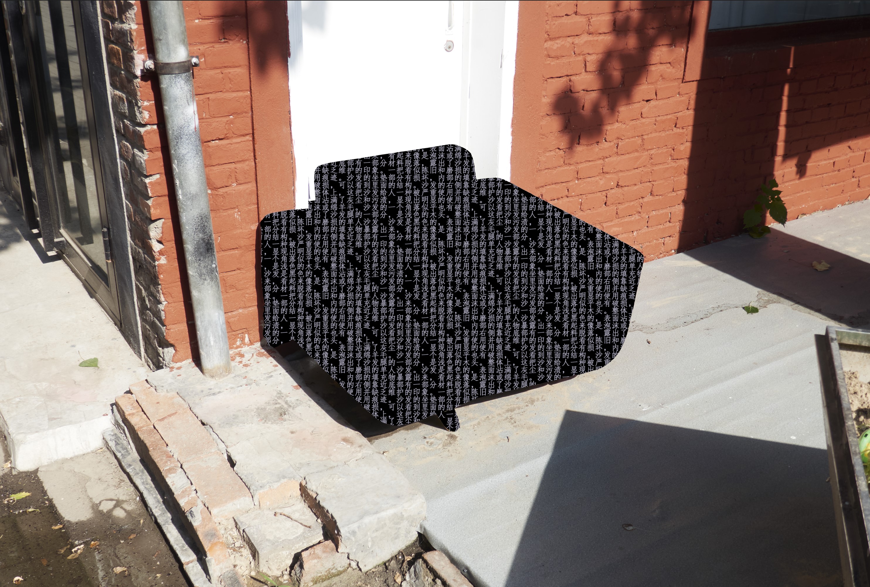 Image of one of Steven's photographs exhibited in his thesis work. The photograph shows an airmchair up against the exterior of a building. The chair has been redacted and is instead shown in black with white Chinese characters that describe the chair.