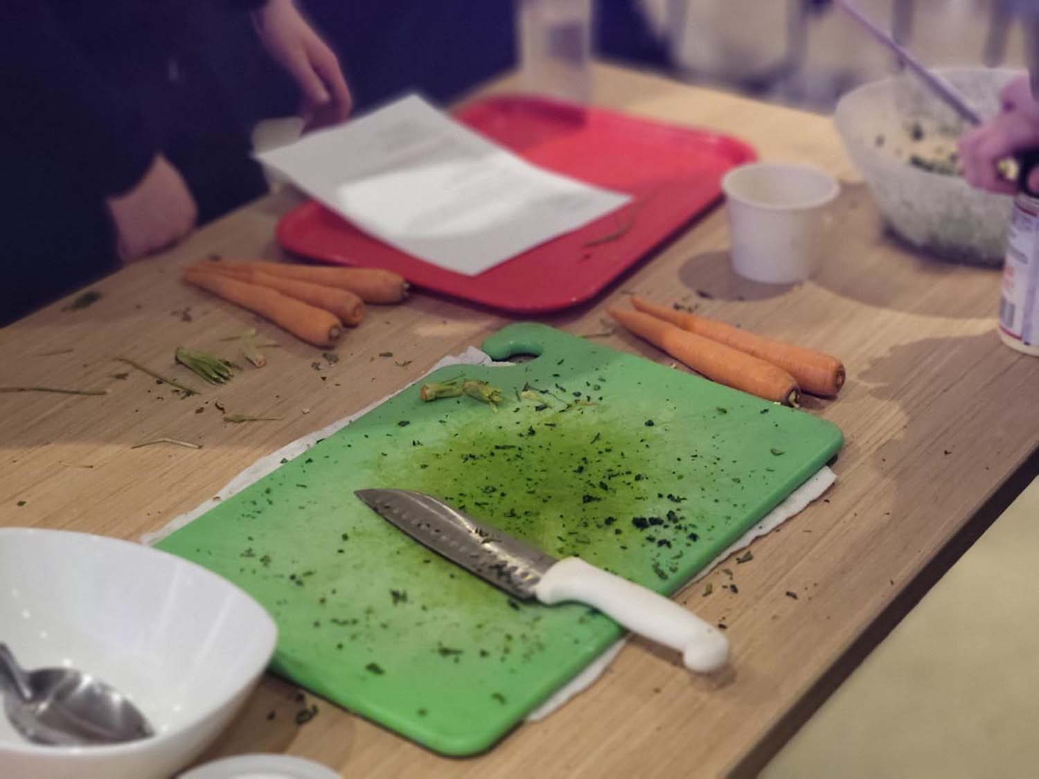 A cutting board sitting on a table with a knife on it. There are several carrots on the table also