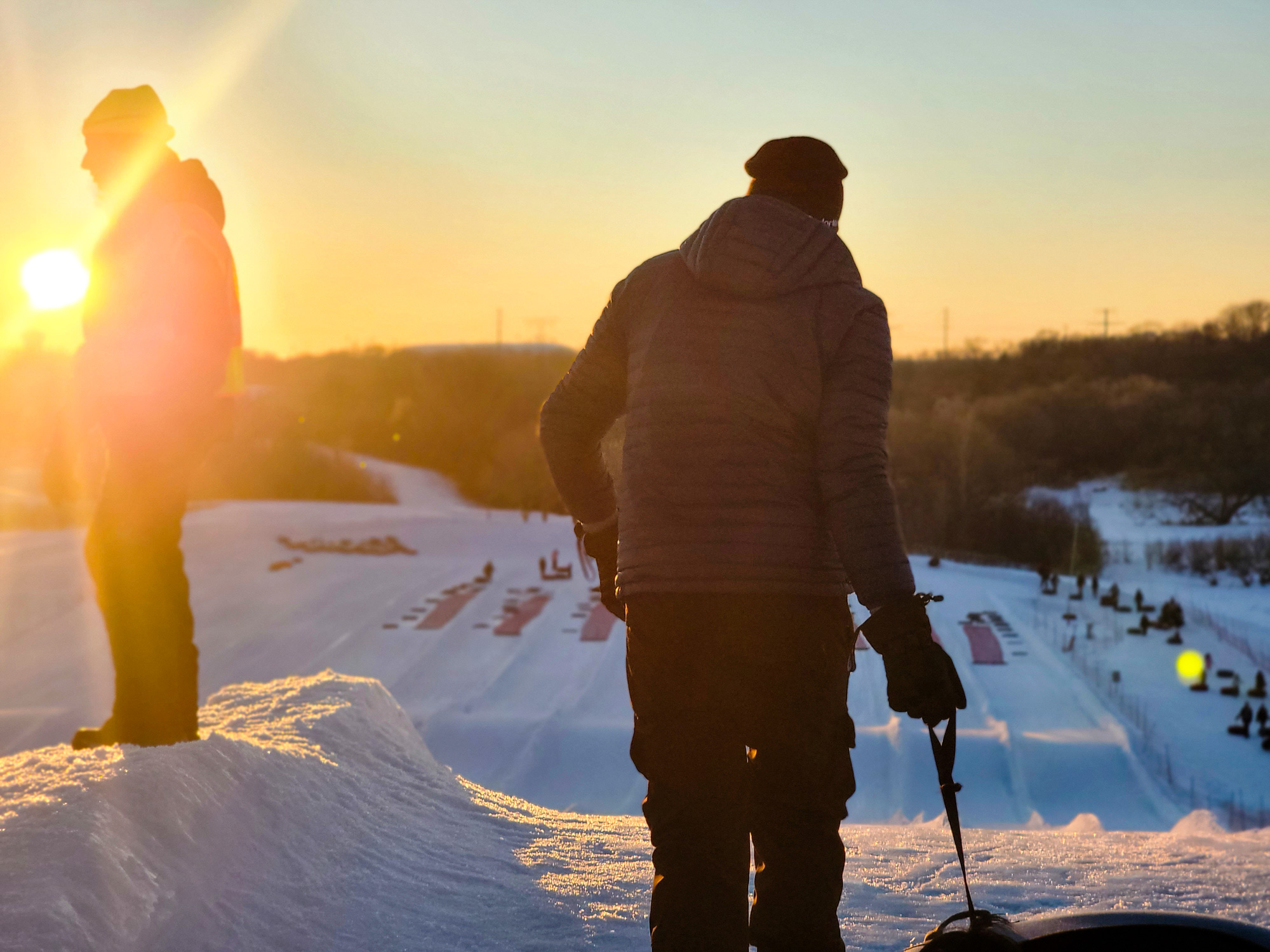 Two people standing on a snowy sledding hill 