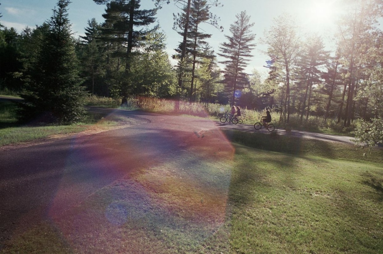 Photograph of a field with trees and bikers in the background