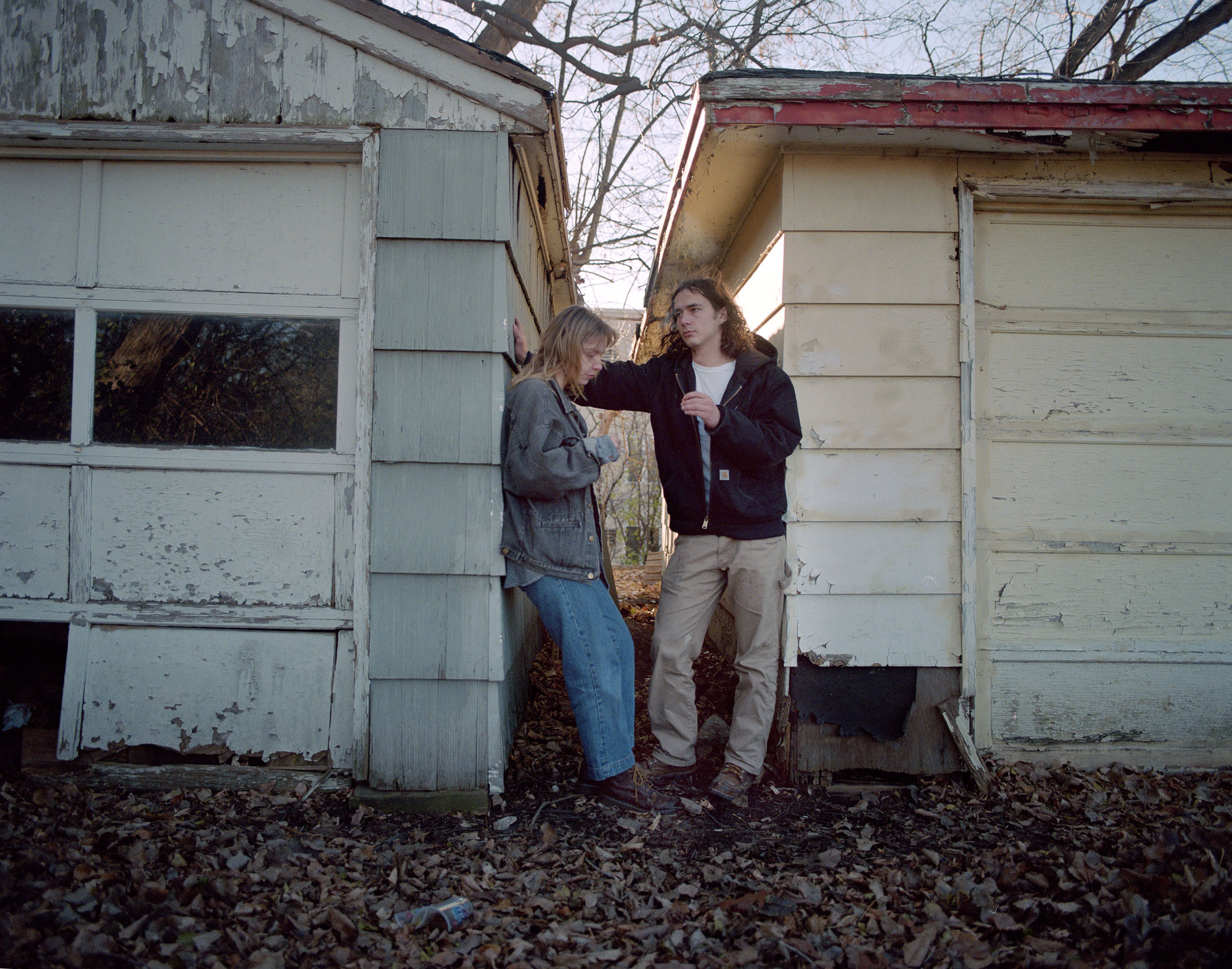 Two young adults talking. They are standing between two sheds.