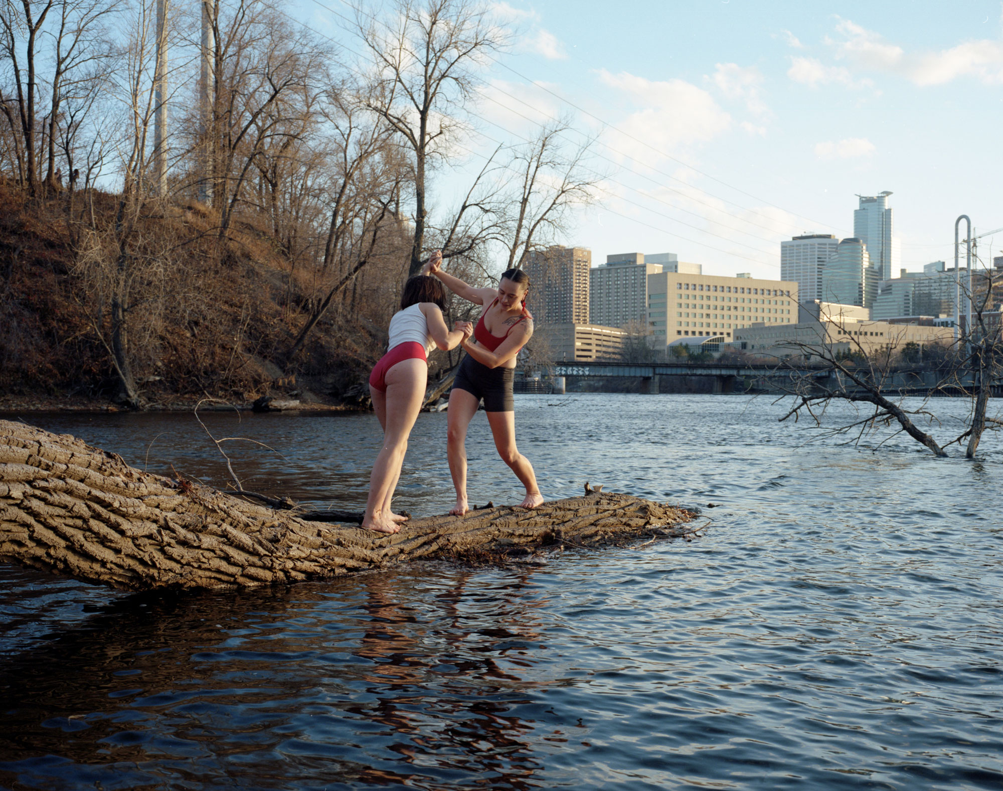 Two young adults on a log over a lake, playfully wrestling