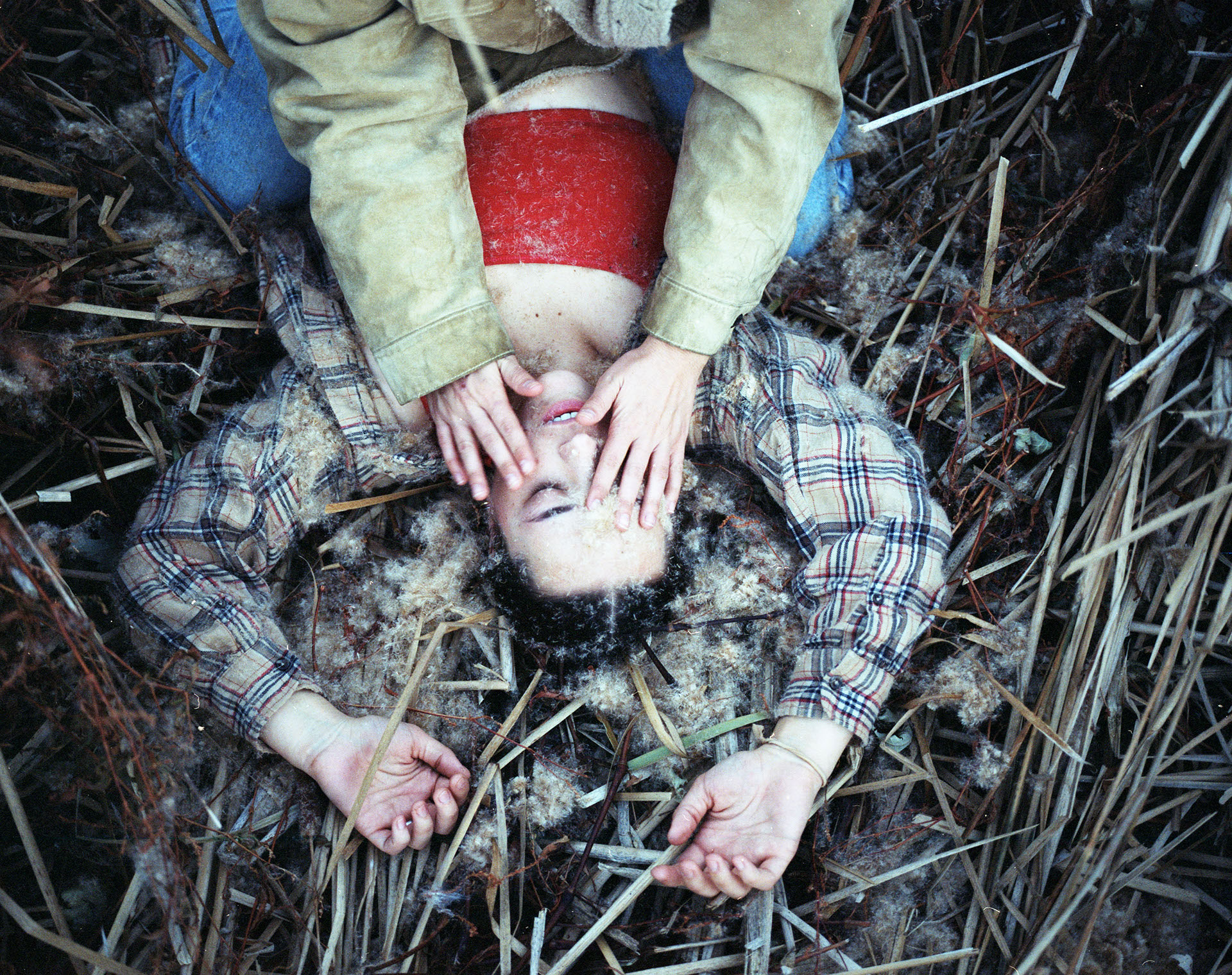 A person laying in a field with another person's hands on their face