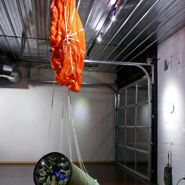 Allison Hiltner, Supply Drop Origins Unknown, 2012, 10,000 cotton swabs, UV emitting light source, UV reactive paint, floral foam, copper, microcrystalline wax, cardboard tube, rubber, plastic, and parachute. 120"h x 65”l x 18"w.