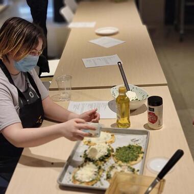 Someone sits at a table putting together a pita bread with greens, beans and feta cheese