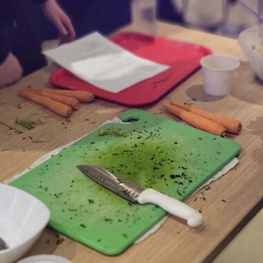A bright green cutting board sits with a knife on-top of it, and several carrots around the board