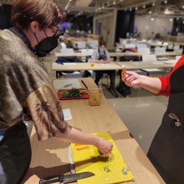 Two people stand around a bright yellow cutting board