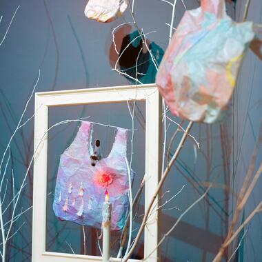 Glimpse of Yi's installation featuring plastic bag form in a frame, thin tree branches, candle and shopping cart