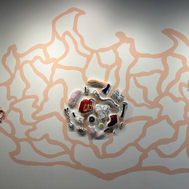 Artwork by Melanie Dowding: an orange-red, abstract painting on a white gallery wall. Several fabric sculptures are installed over the mural.