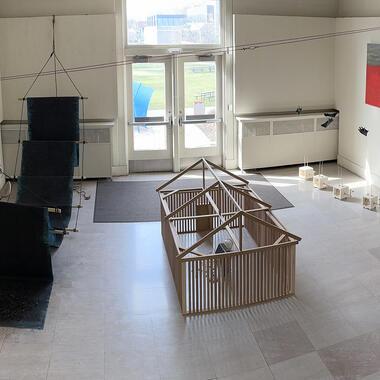 Image of Victor's thesis installation in the Morrison Building. Included are sculptures that are in part made of wood, paper, and charcoal. There is a grey and red painting on the far wall.