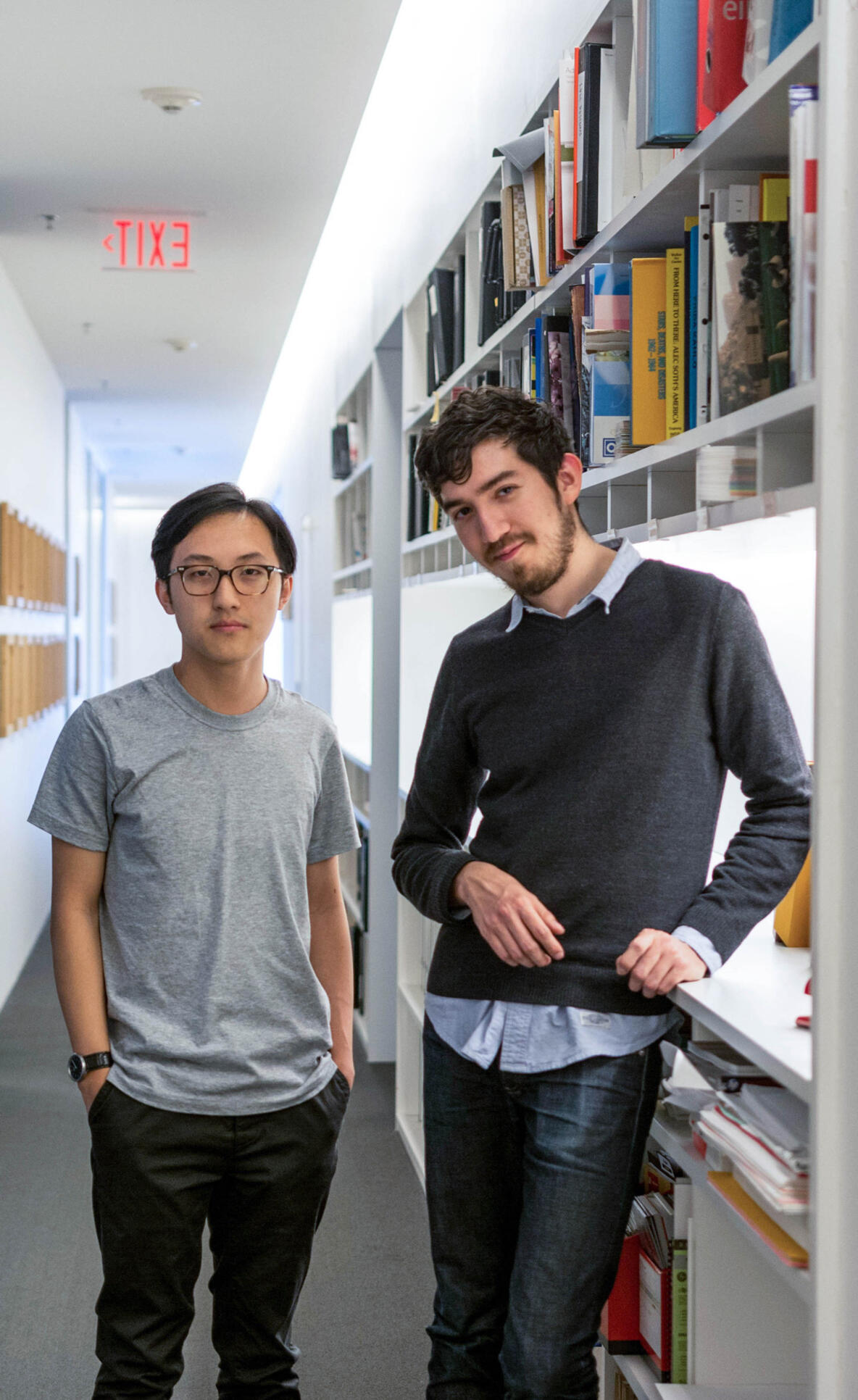 Two students standing in a room with bookshelves behind them