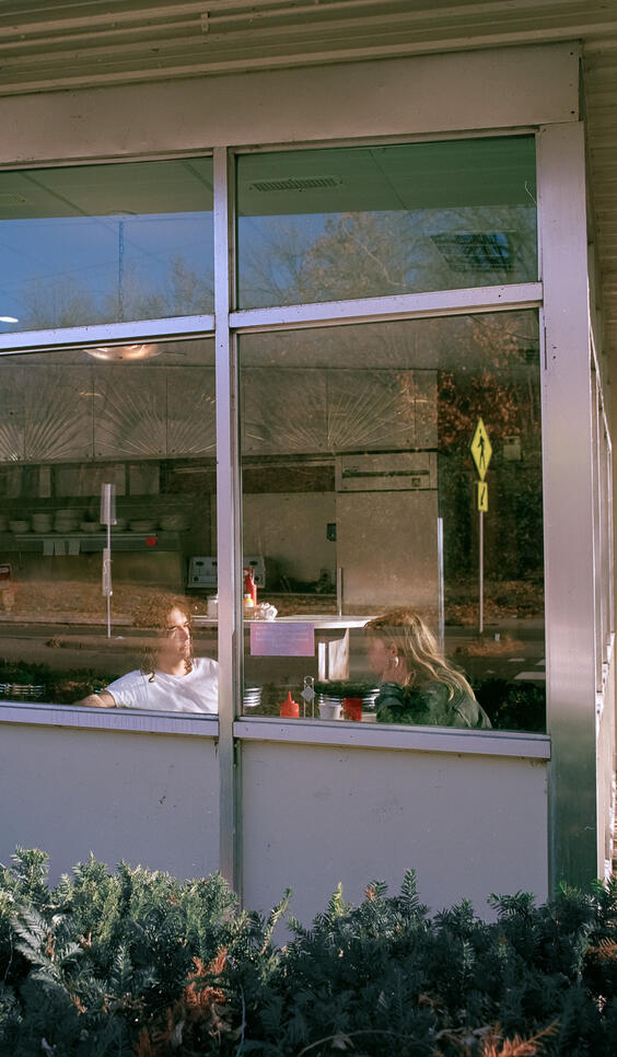 Two people eating in a diner, viewed through a window ; London King