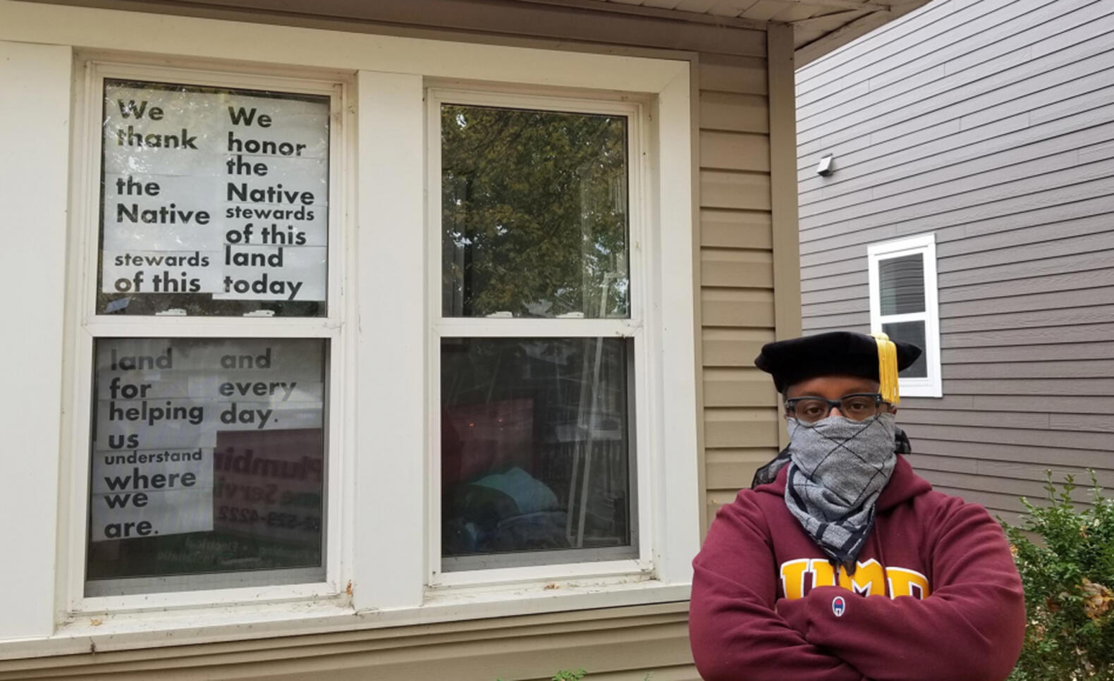 Man standing in front of window where signs read messages about thanking the Native population ; George Hoagland