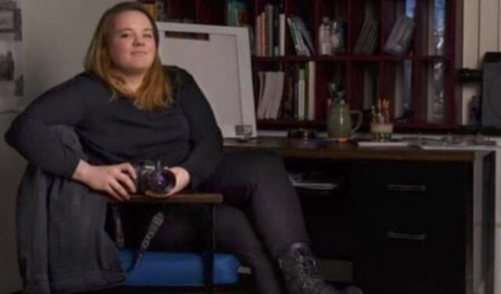 Gallery Director Cassandra Cook seated in chair holding camera.