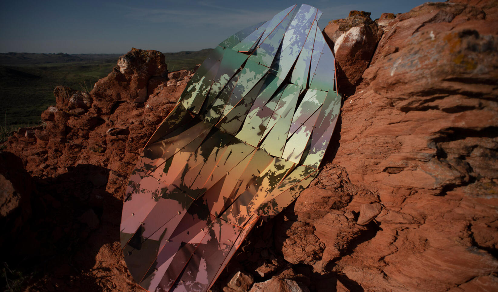Large piece of holographic geometric appearing metal ontop of a red cliffside ; David Andree