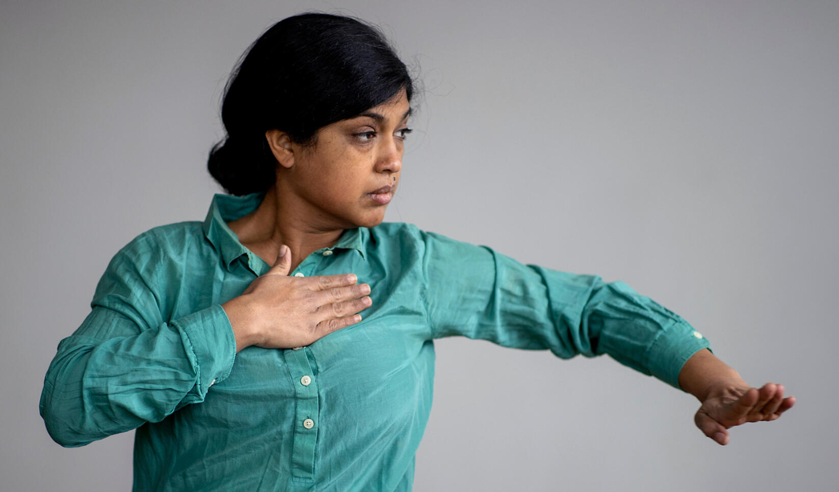 Pramila Vasudevan dancing in a cyan shirt against a grey background