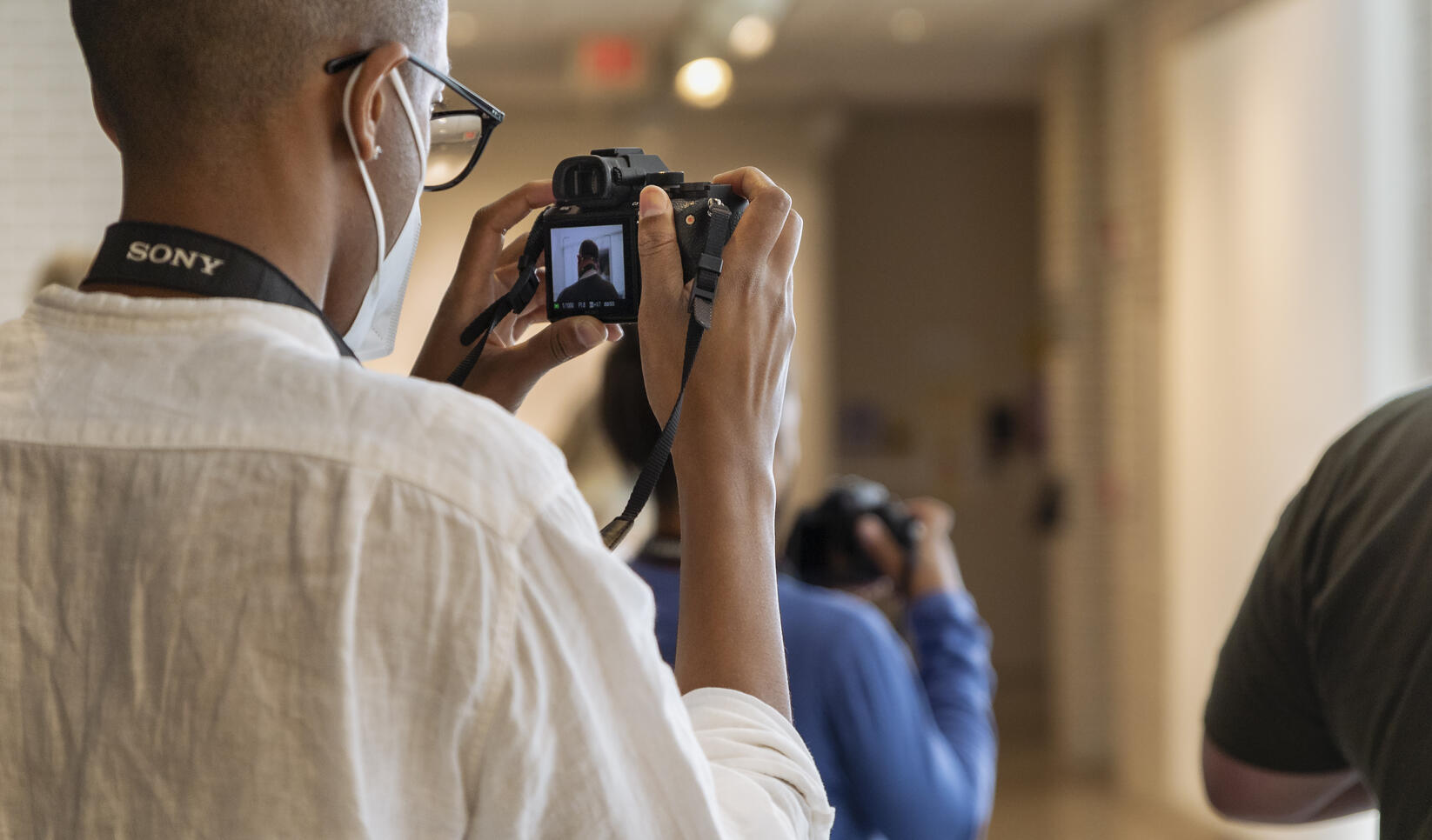 Student seen from behind looking into a camera viewfinder.