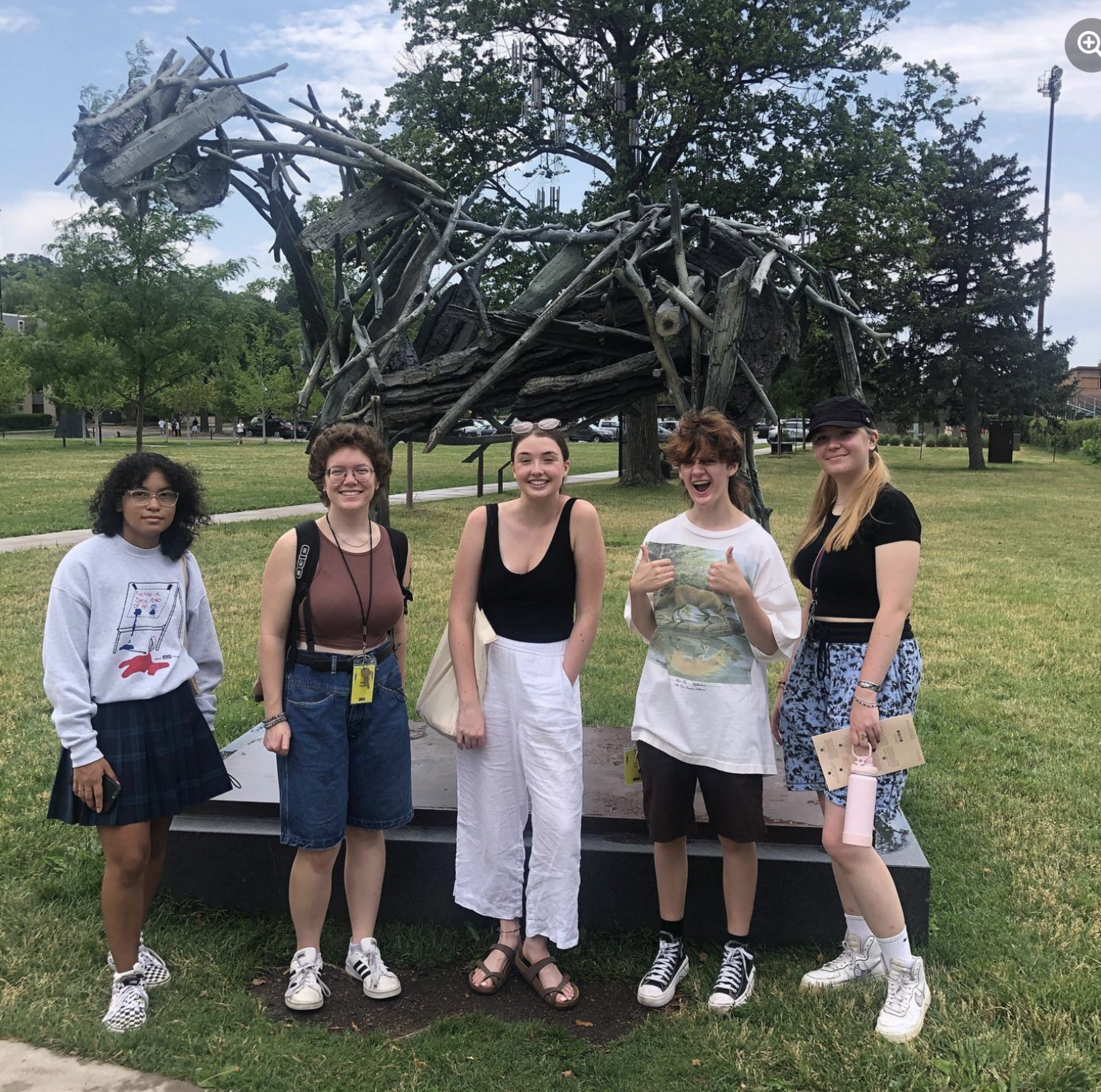 Group of five students stand outside in front of an abstract horse sculpture made out of pieces of wood.