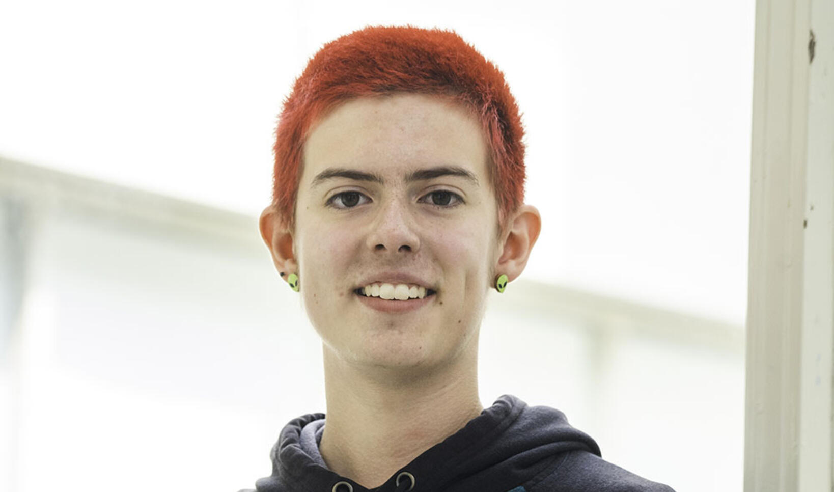PCSS student standing in front of a white background with red hair and a hoodie.