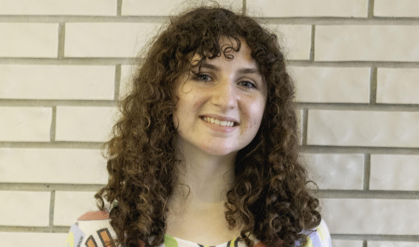 PCSS student standing in front of white wall wearing their hair down with a colorful shirt