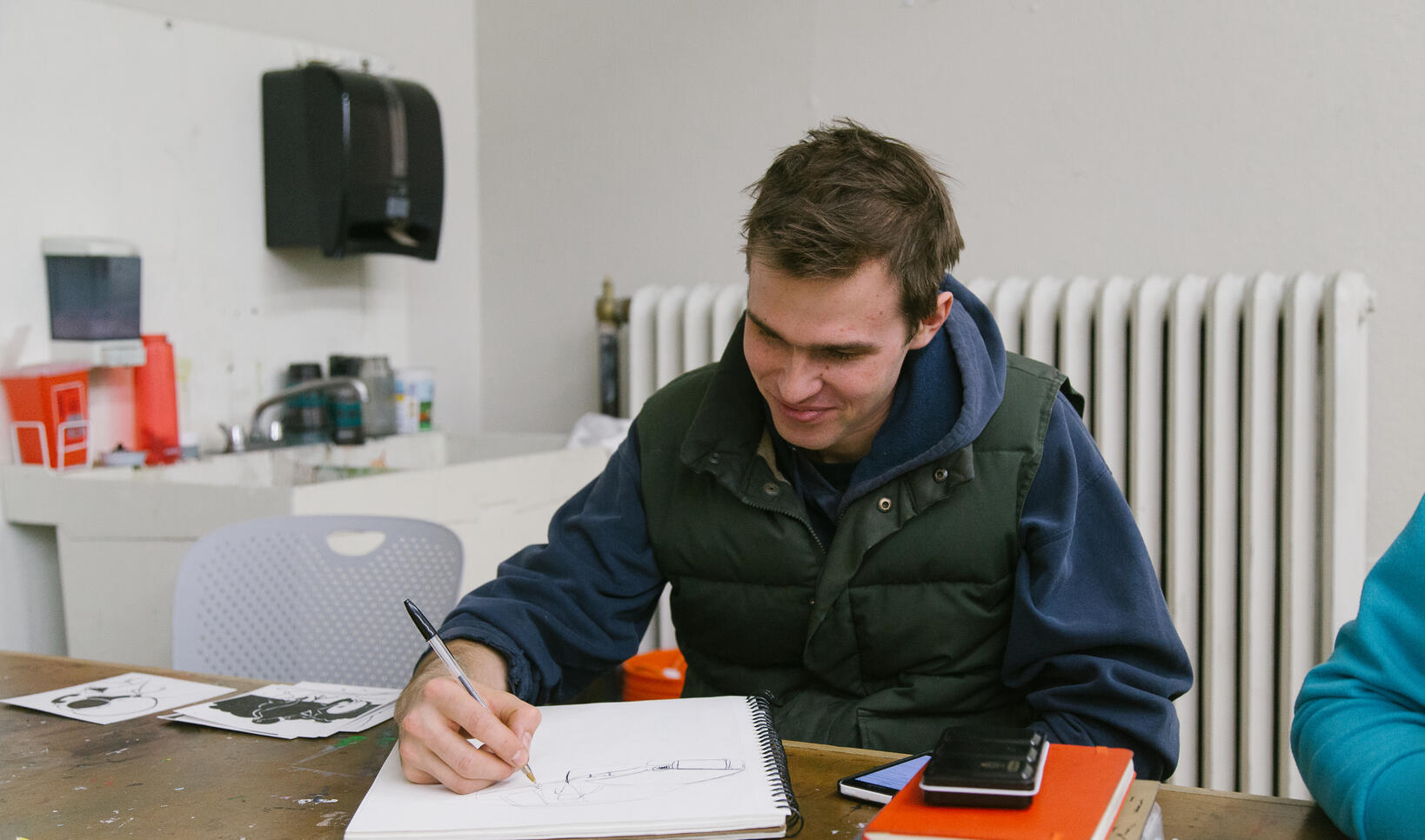 Student sits at a table and draws in a sketchbook.