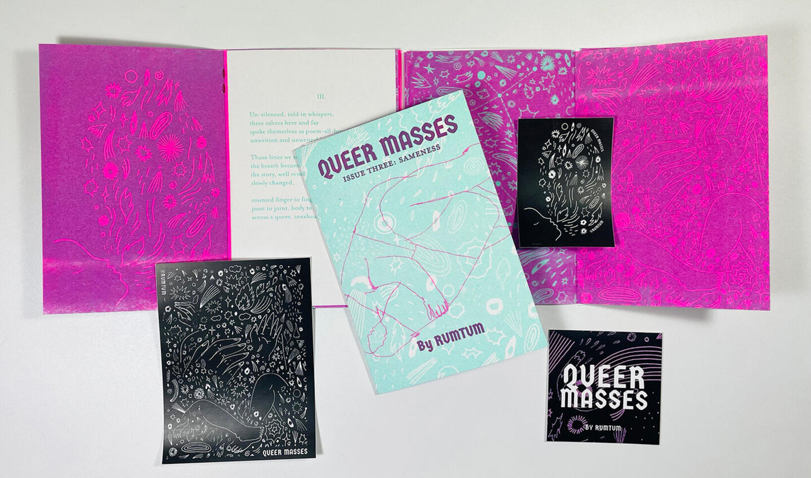 The zine "Queer Masses" is displayed with several other merchandise items around it