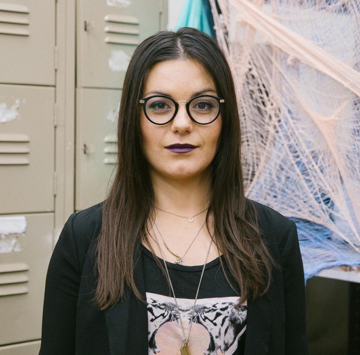 Portrait of Janie Arguedas. She is standing in front of material used for one of her exhibitions.