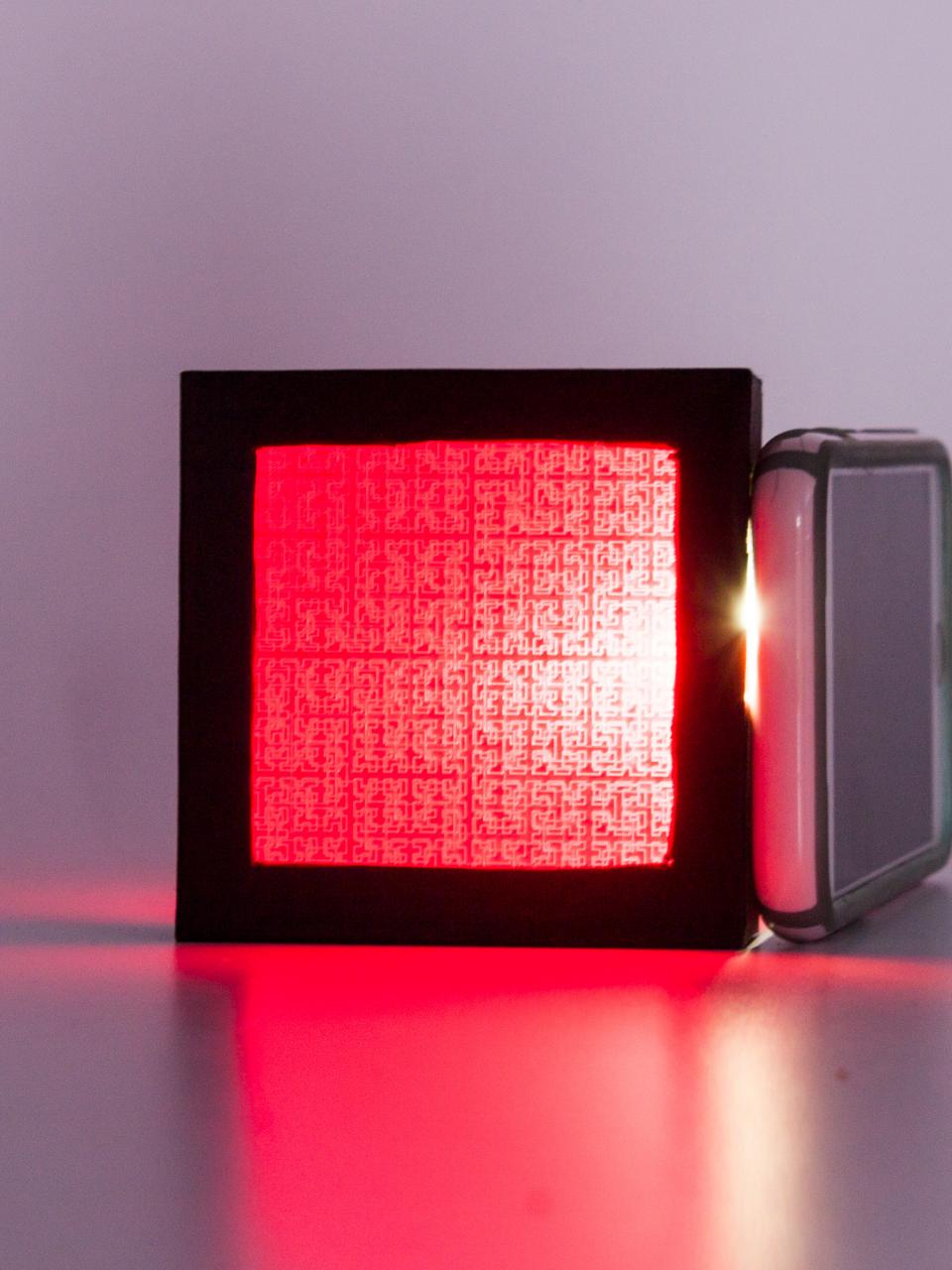 A black frame captures a red screen in which the light source behind it exposes a printed pattern.