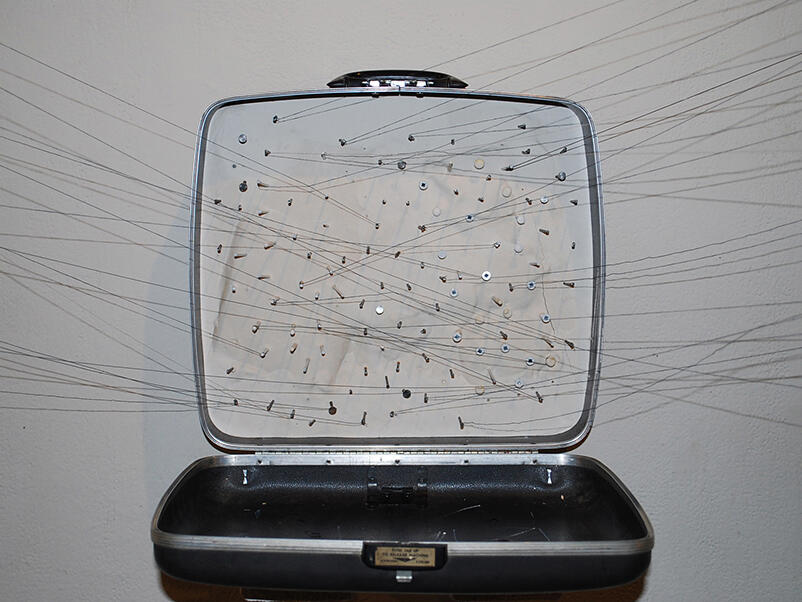 Mixed media sculpture composed of a suitcase, string, and other found materials.