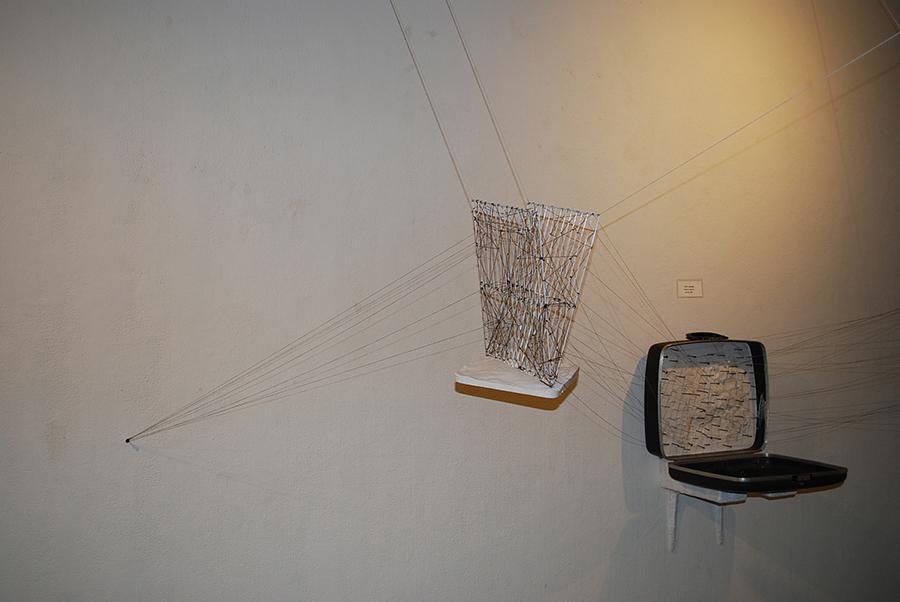 Mixed media sculpture composed of a suitcase, string, and other found materials.