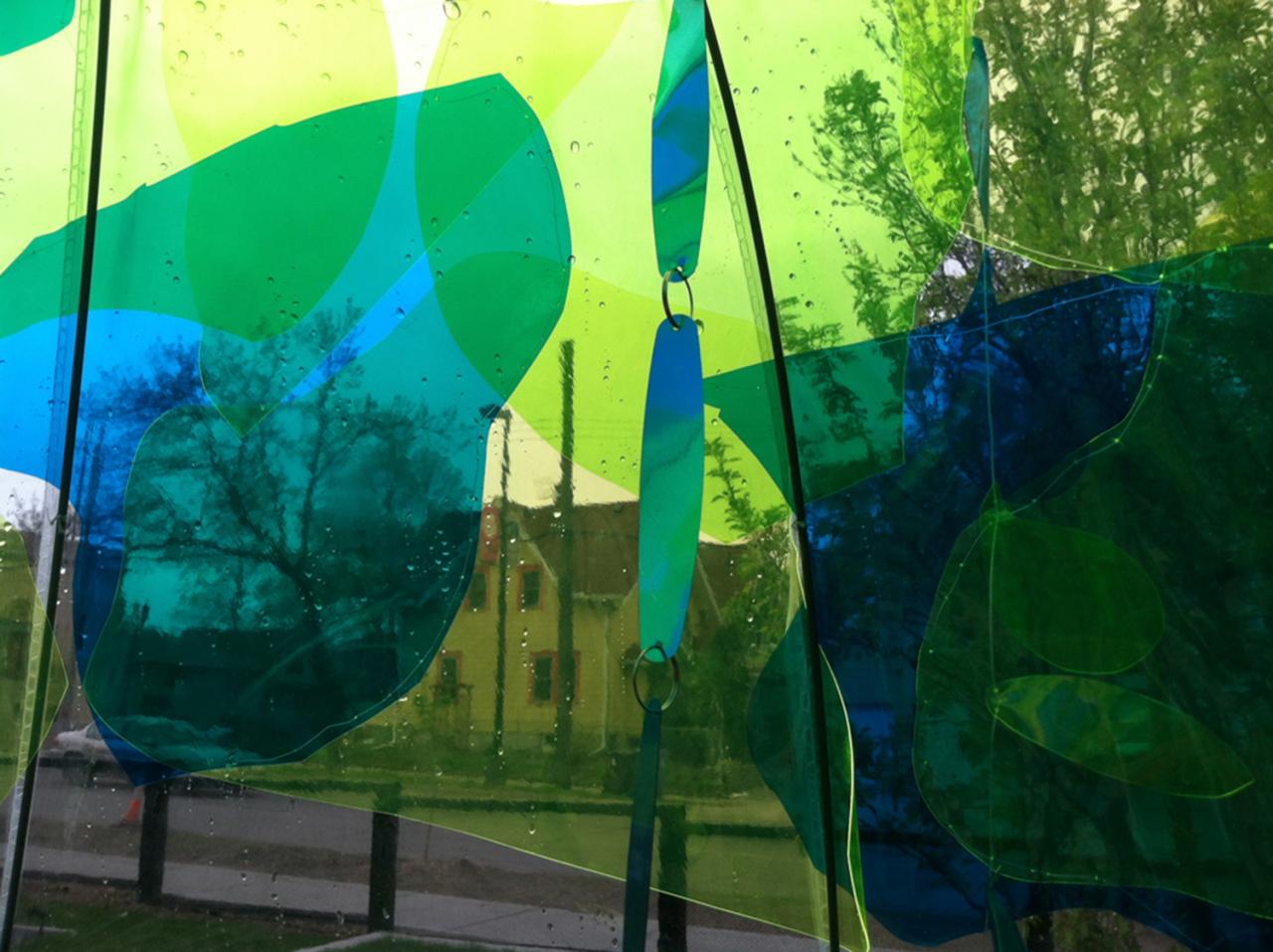 Public sculpture featuring sheets of blue and green, catching light. 