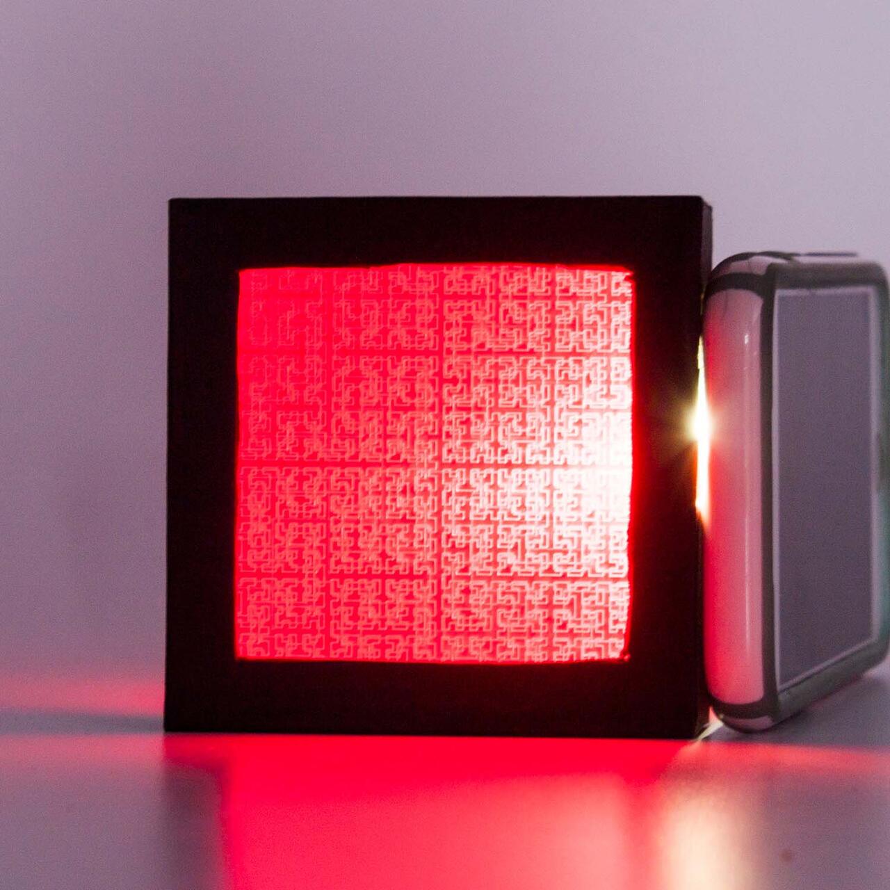 A black frame captures a red screen in which the light source behind it exposes a printed pattern.