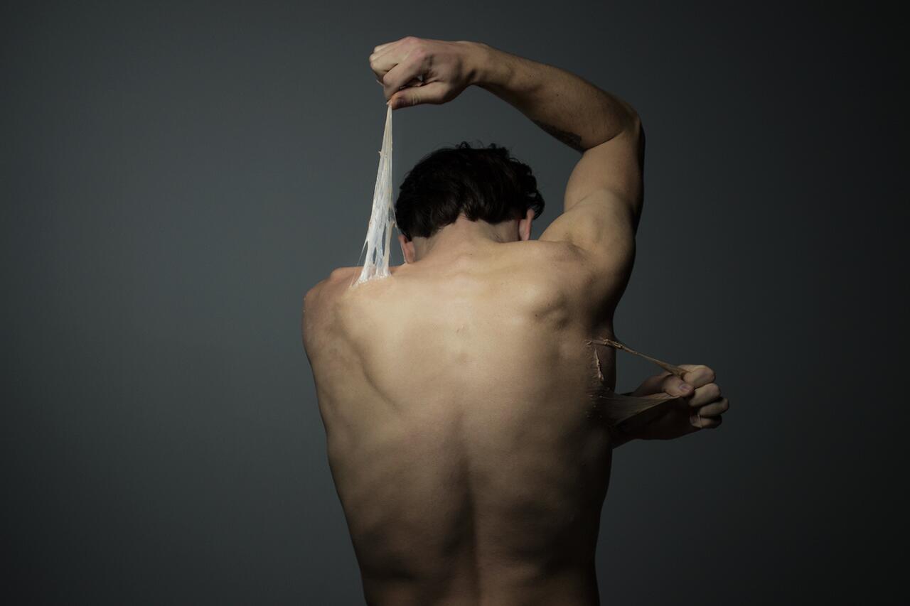 Dramatic portrait photograph of a figure pulling at their skin.