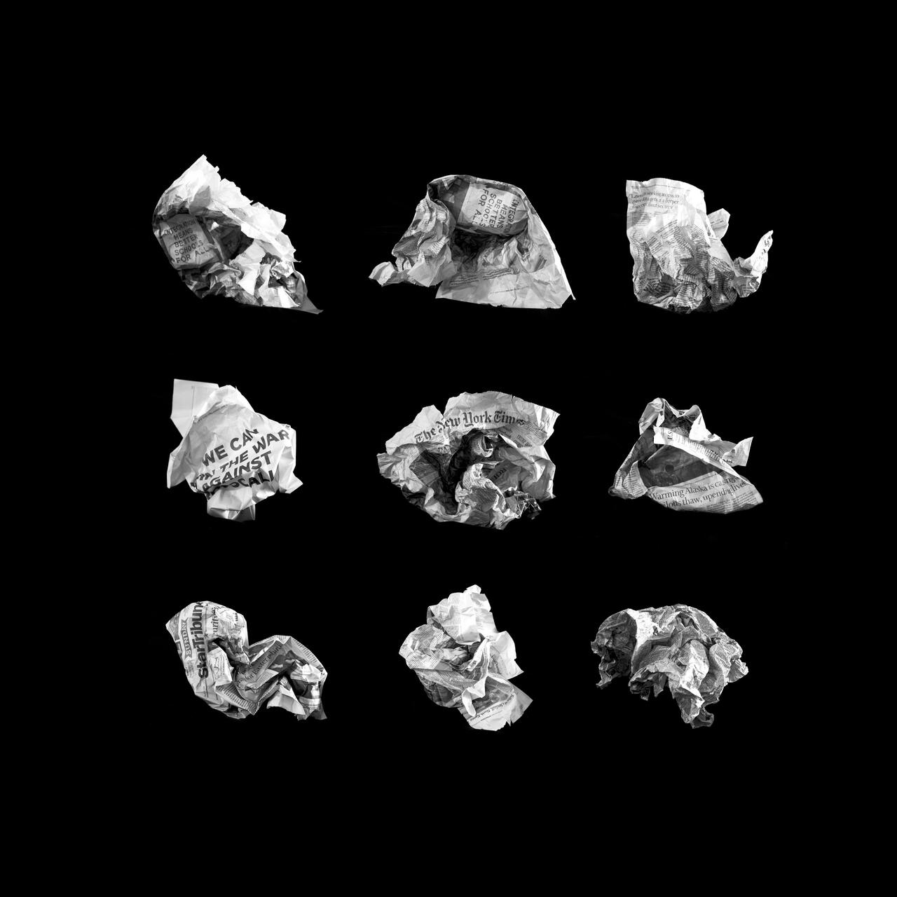 Grayscale photograph featuring nine crumpled pieces of newspapers. 
