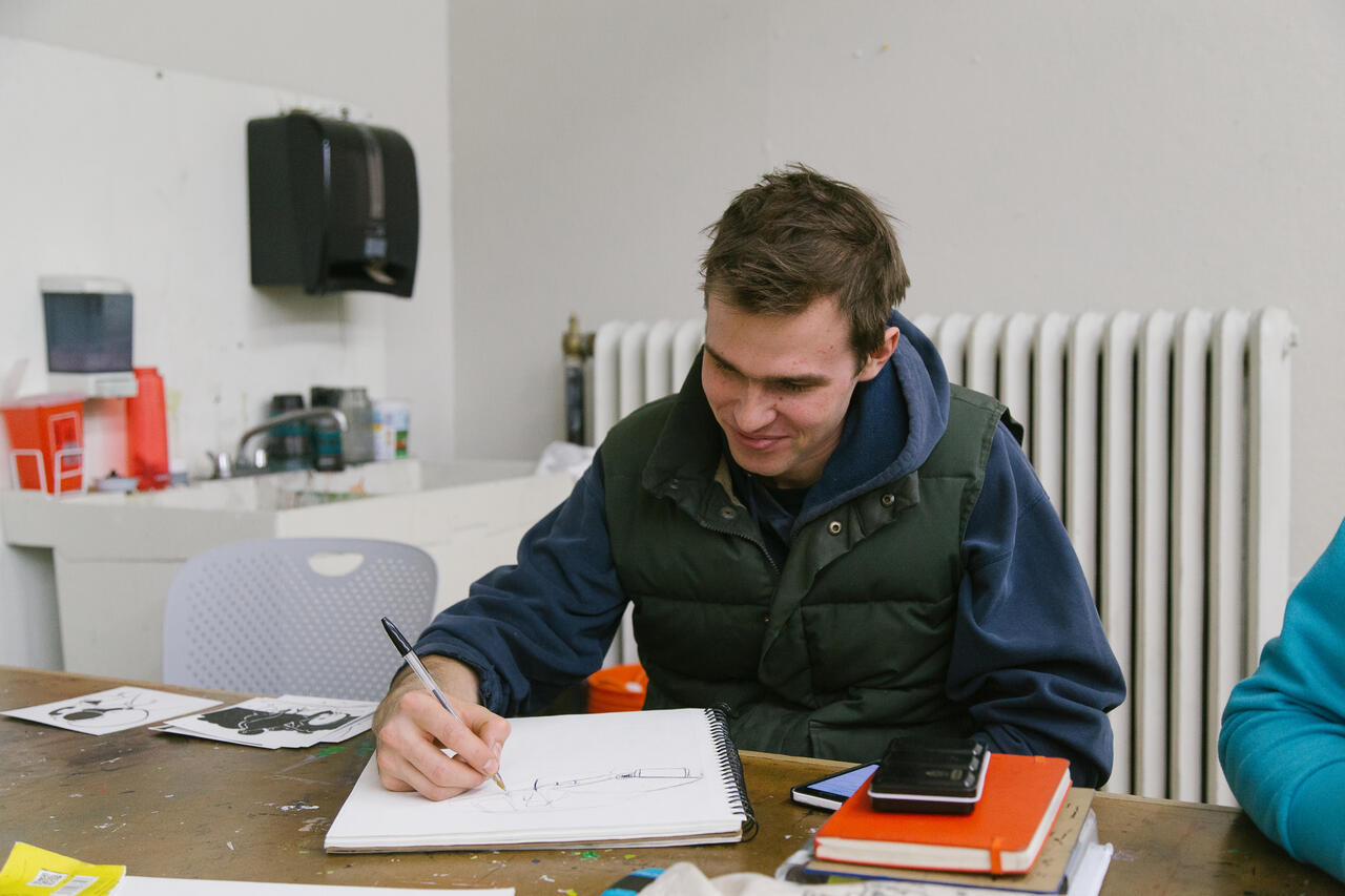 Student sits at a table and draws in a sketchbook.