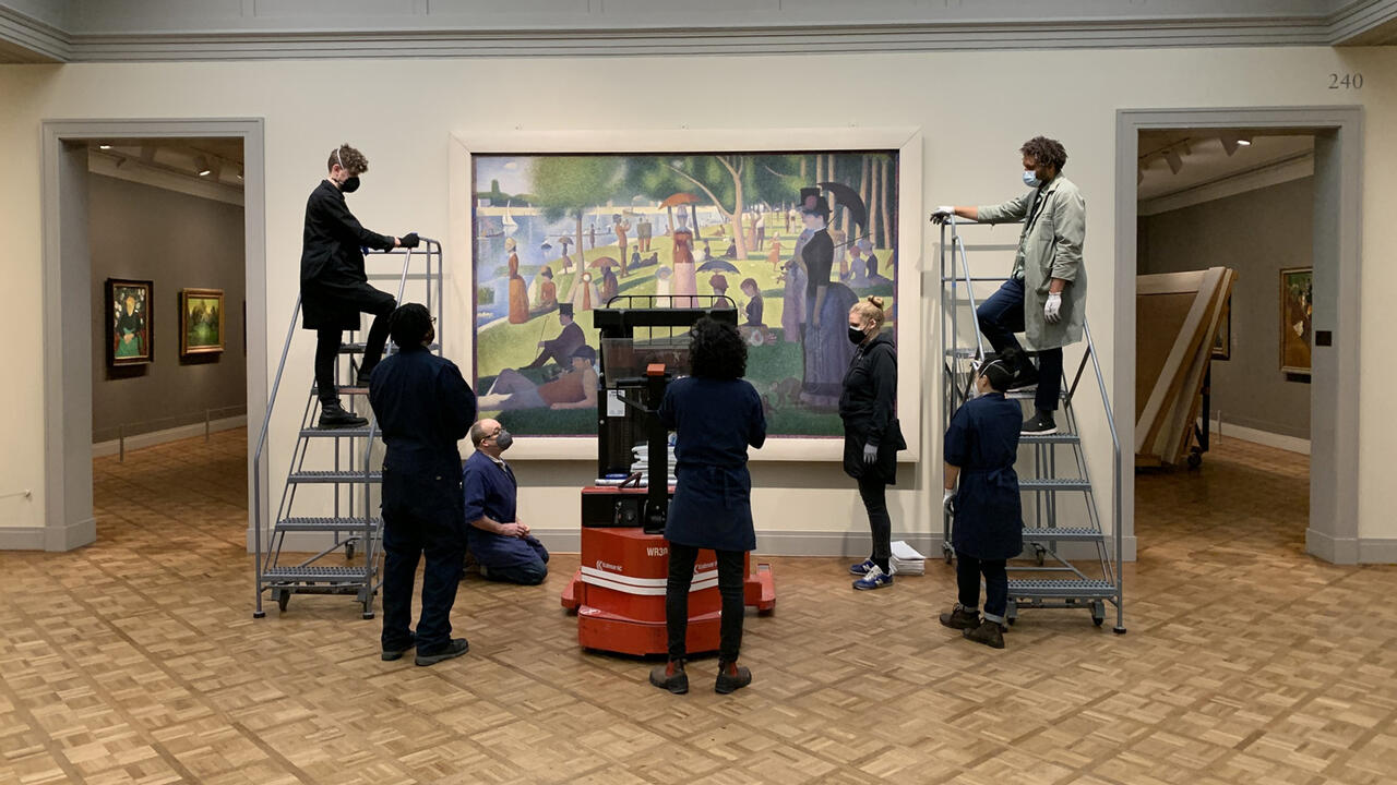 Several people gathered around the painting "A Sunday Afternoon on the Island of La Grande Jatte" all putting a frame onto it