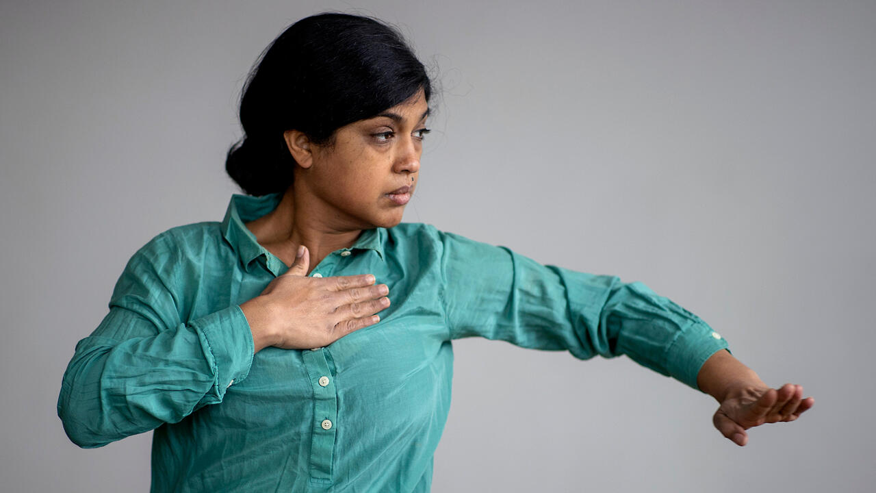 Pramila Vasudevan dancing in a cyan shirt against a grey background
