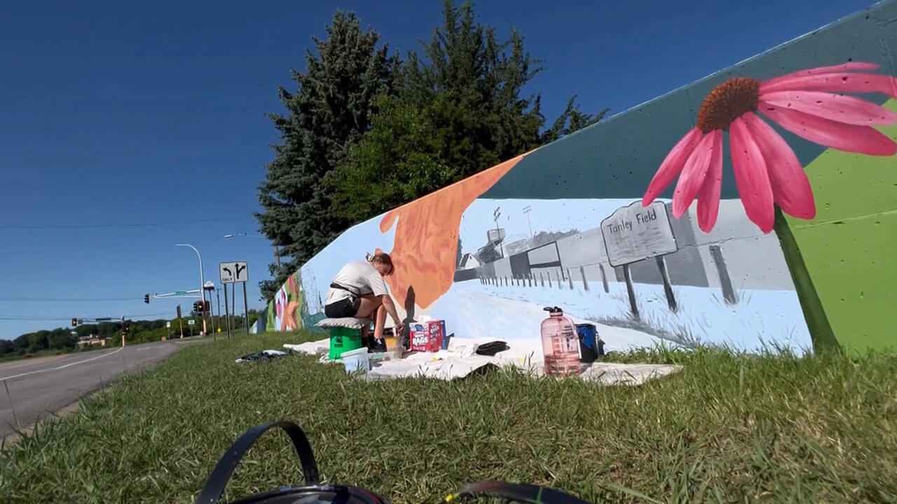 Someone sits on a tarp painting a mural by the roadside