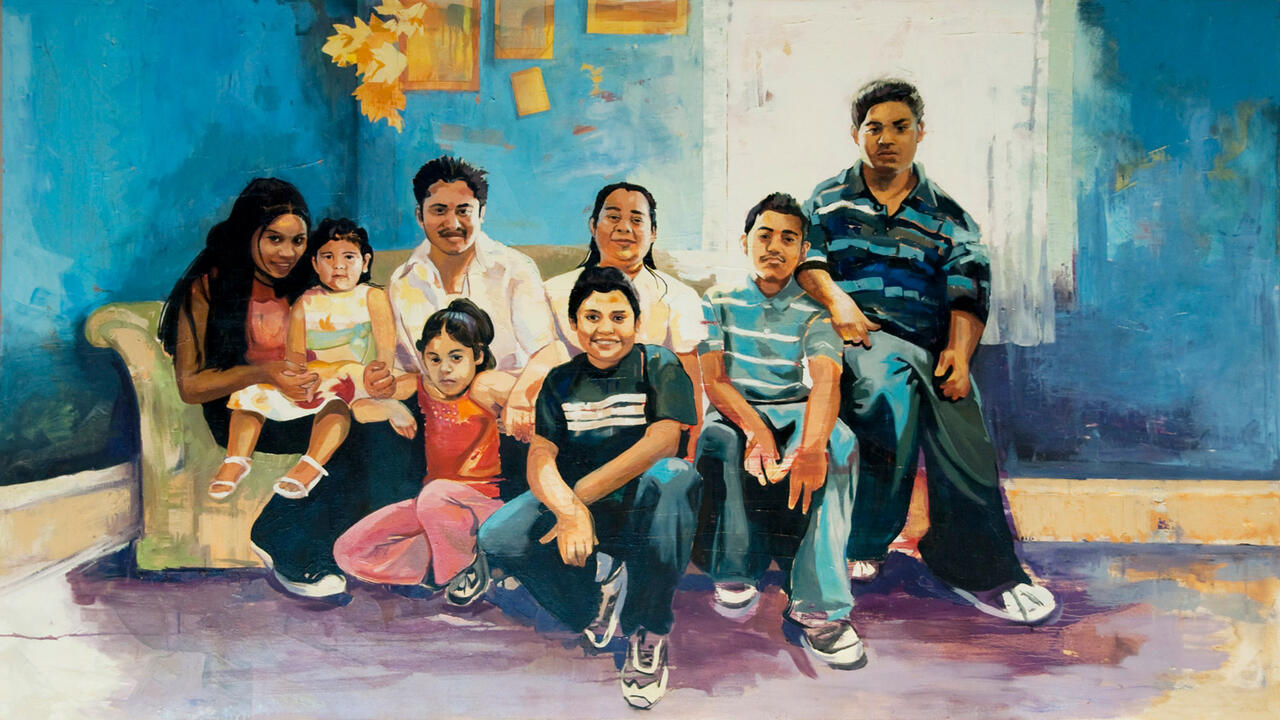 A painting of a family, there are eight members, some sitting on the ground, some sitting on a couch, they are all smiling and the walls in the back are a bright blue