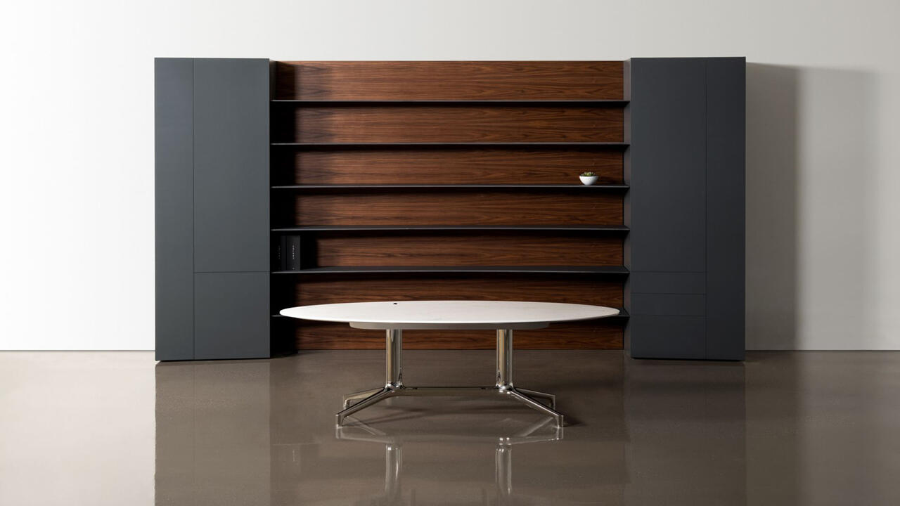 A table made up of metal geometric legs and a sleek white table top sits in the middle of an empty room
