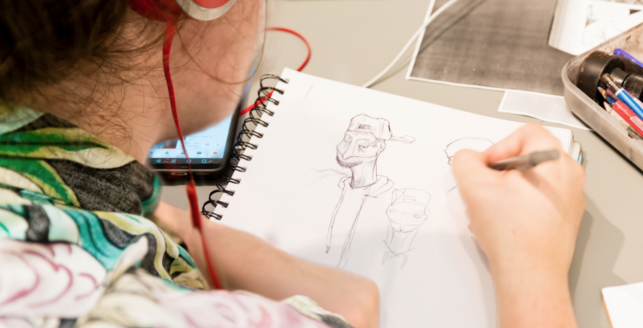Student draws character in sketchbook with pencil.