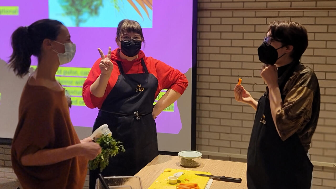 Three people stand around a table covered in cooking ingredients