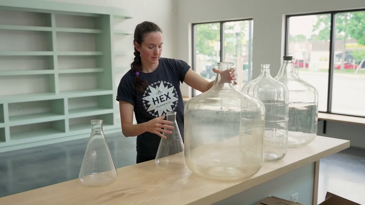 Image of a woman organizing blank bottles on a countertop in a relatively empty store space.