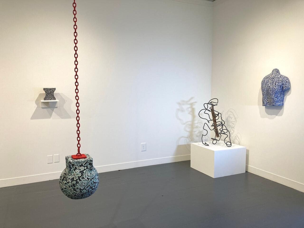 An image of an art installation, including a porcelain wrecking ball, a porcelain woman's chest, a porcelain vase on the wall, and a wire piece.