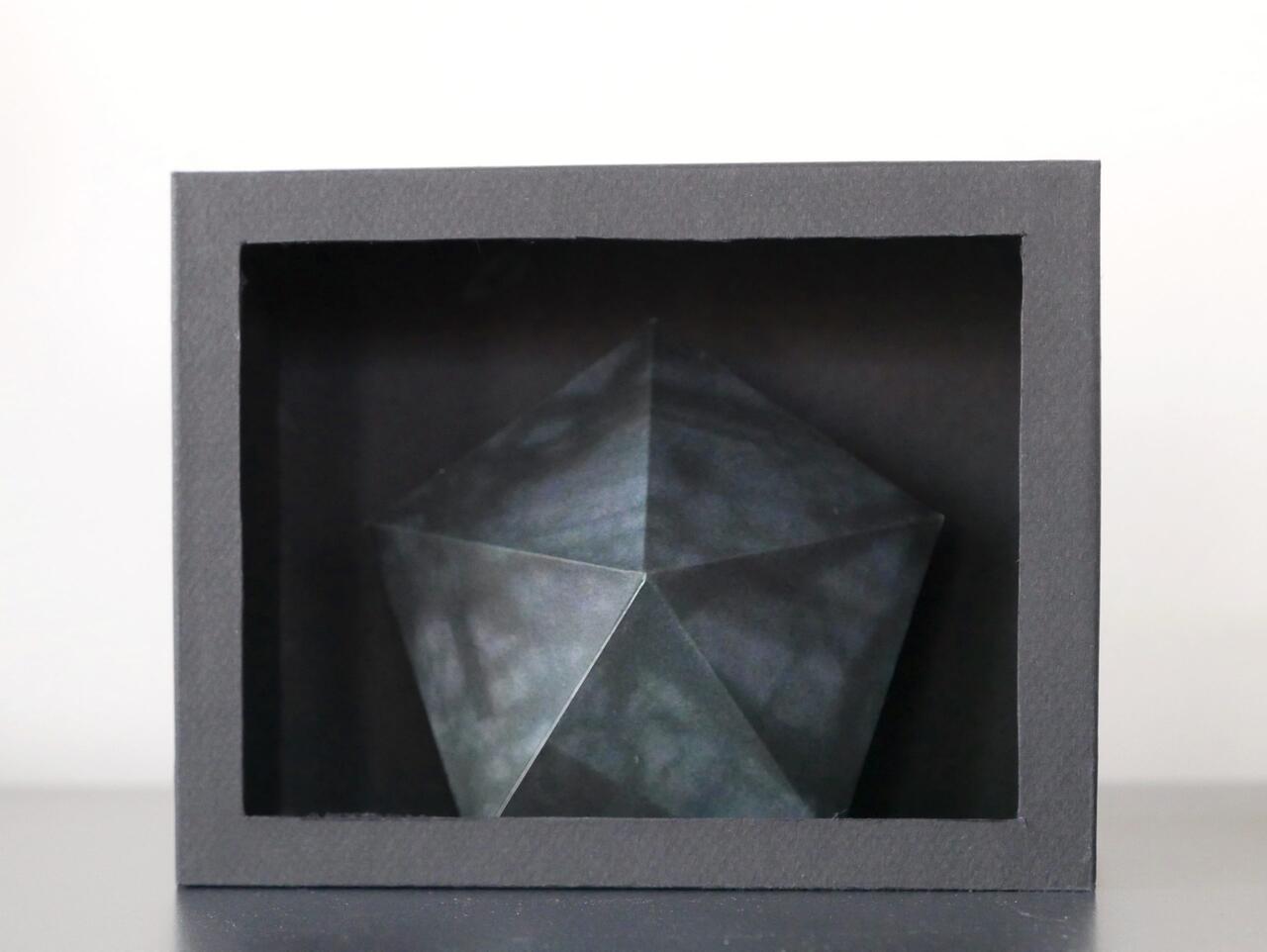 An image of a gray box with a dark gray textured pentagonal prism inside.