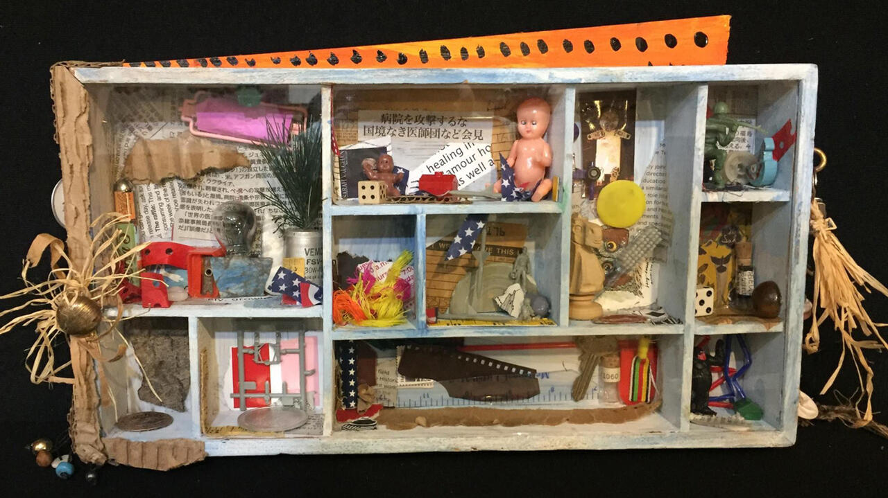 A small miniature of a white shelf filled with small trinkets such as figures of babys, wrapping papers, and other small objects