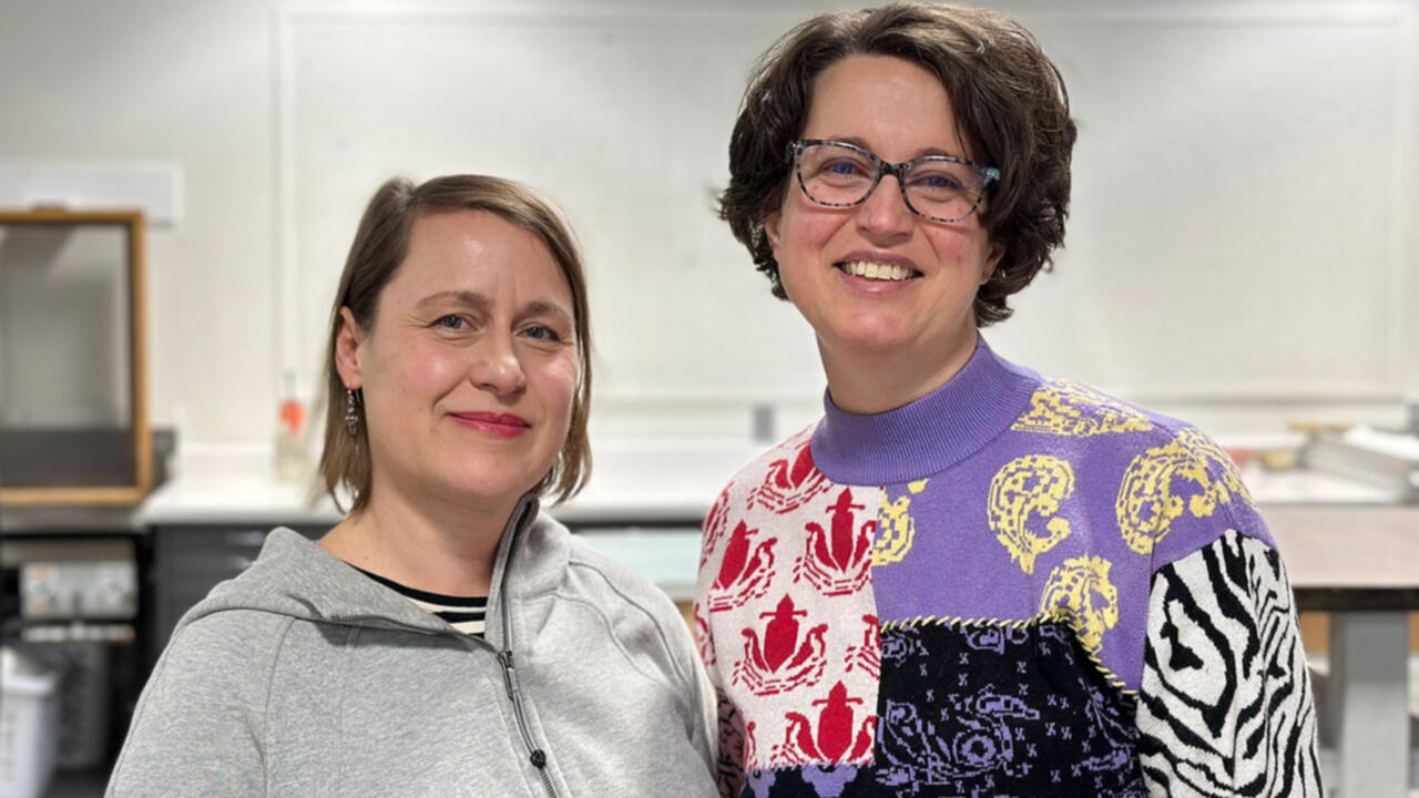 Two women are standing next to eachother looking into the camera and smiling.