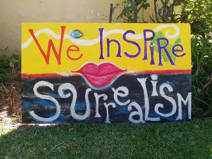 A yard sign painting with "We InsPiRe SurreaLisM" in a surreal font on it