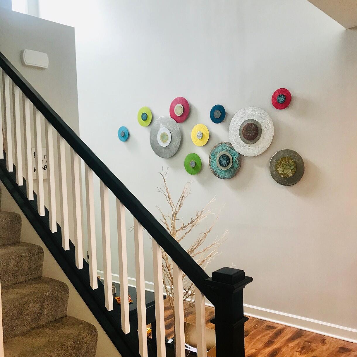 Multicolored disks mounted onto a wall, the disks are a range of red, blue, green and yellow and all contain smaller disks inside of them