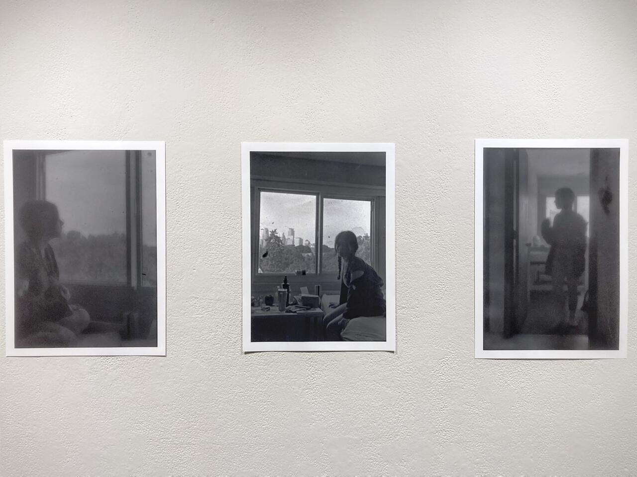 Three black and white photographs. Central image shows a student sitting in her dorm room, by a window and is in clear focus. Image on the left also features the student sitting by a window but is out of focus. Image on the right shows the student standing in the doorway and is also out of focus.